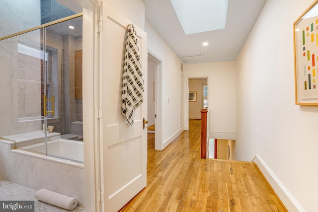 corridor with an upstairs landing, wood finished floors, recessed lighting, baseboards, and a skylight