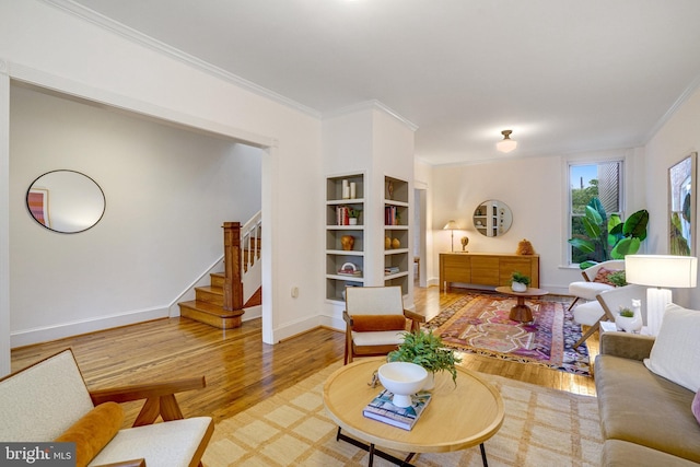 living area featuring ornamental molding, stairs, wood finished floors, baseboards, and built in shelves
