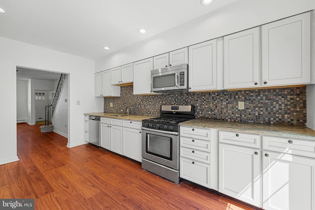 kitchen with appliances with stainless steel finishes, tasteful backsplash, wood finished floors, white cabinetry, and baseboards