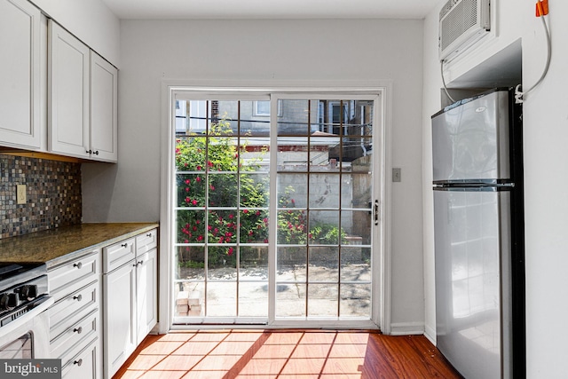kitchen featuring appliances with stainless steel finishes, tasteful backsplash, white cabinets, a wall mounted AC, and light wood-type flooring