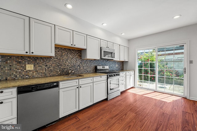kitchen with stainless steel appliances, a sink, dark wood-style floors, backsplash, and white cabinets