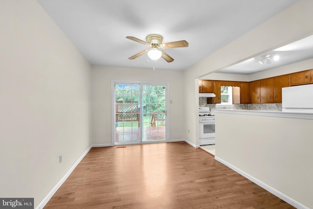 unfurnished living room with ceiling fan, light wood-type flooring, and baseboards