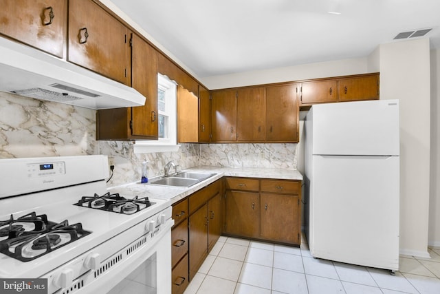kitchen with white appliances, a sink, under cabinet range hood, and brown cabinets