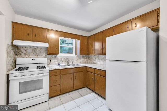 kitchen featuring white appliances, under cabinet range hood, a sink, brown cabinets, and tasteful backsplash