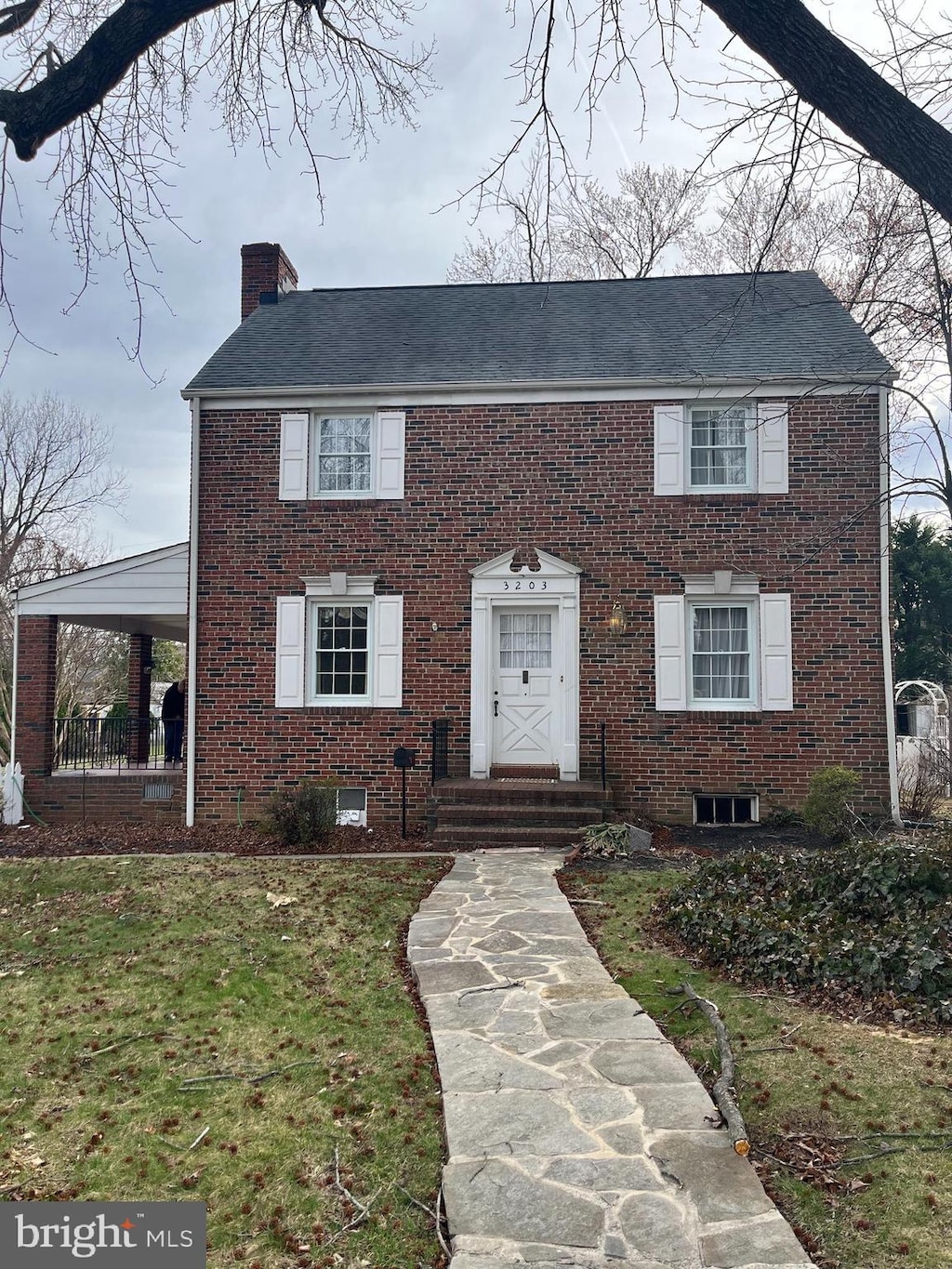 colonial home with a chimney, brick siding, and a front yard