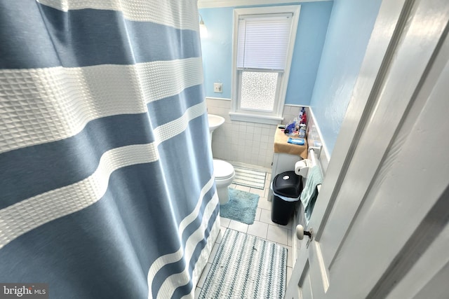 bathroom featuring tile walls, tile patterned flooring, a wainscoted wall, and toilet