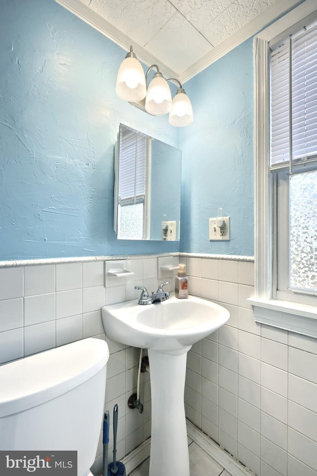 half bath with tile walls, a textured wall, crown molding, and toilet
