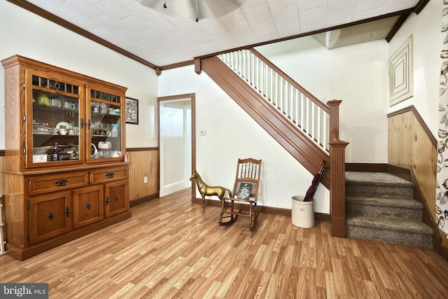 living area with crown molding, light wood-style floors, stairs, a wainscoted wall, and baseboards