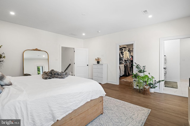 bedroom featuring wood finished floors, recessed lighting, a spacious closet, and baseboards