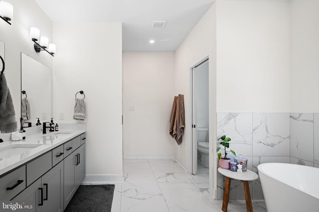 full bathroom with marble look tiles, a freestanding tub, recessed lighting, double vanity, and toilet