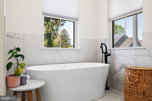 bathroom featuring tile walls, marble look tiles, plenty of natural light, a freestanding tub, and wainscoting