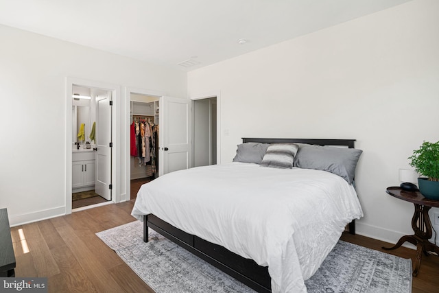 bedroom featuring baseboards, wood finished floors, a walk in closet, a closet, and connected bathroom
