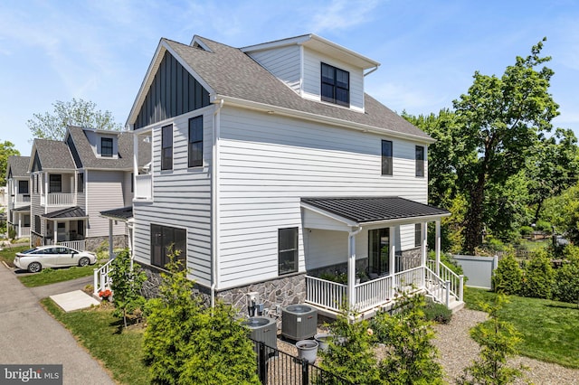 view of side of property featuring stone siding, cooling unit, covered porch, and board and batten siding