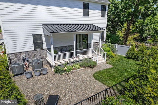 rear view of property with a standing seam roof, cooling unit, stone siding, and metal roof