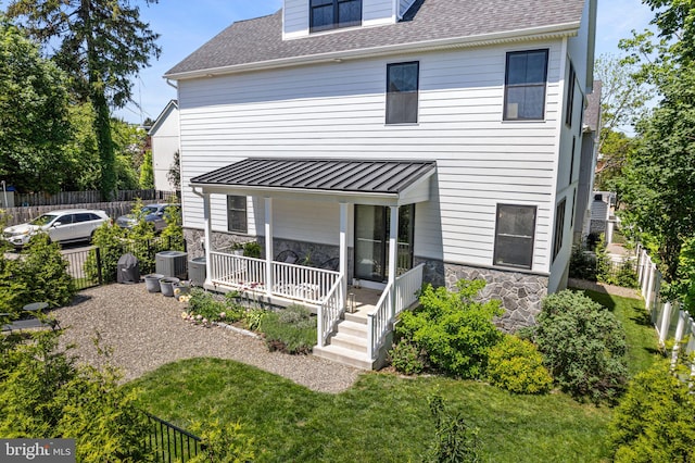 back of house with stone siding, covered porch, central AC unit, and fence
