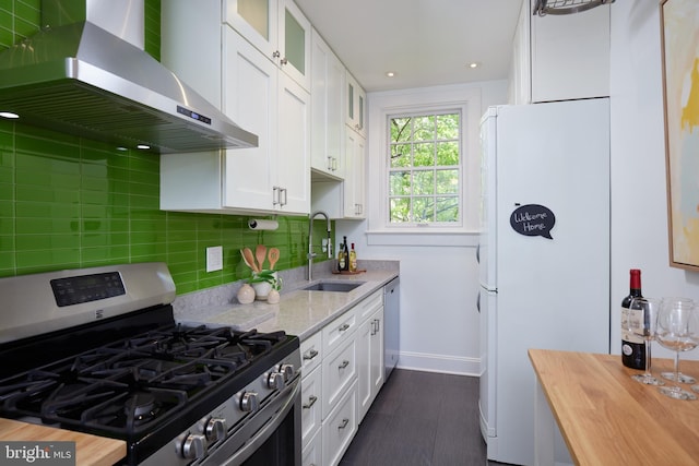 kitchen with stainless steel gas range oven, wall chimney exhaust hood, freestanding refrigerator, a sink, and white cabinets