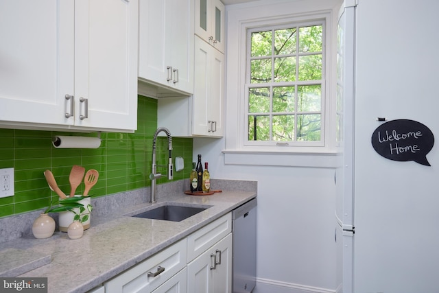 kitchen featuring a sink, dishwasher, white cabinets, freestanding refrigerator, and decorative backsplash