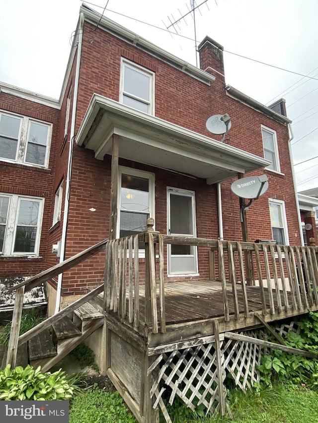rear view of house with brick siding, a deck, and a chimney