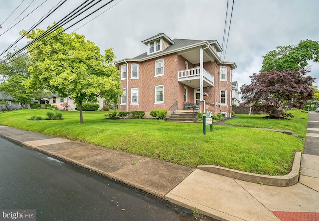 view of front of house featuring a balcony, brick siding, and a front yard