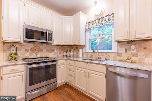 kitchen with stainless steel appliances, a sink, wood finished floors, and light stone counters