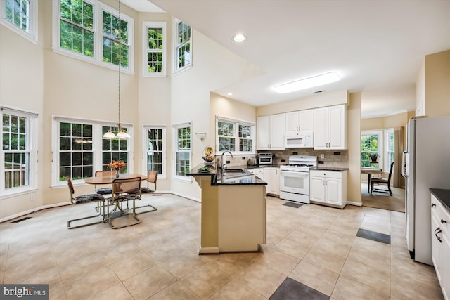 kitchen featuring white appliances, a sink, dark countertops, a peninsula, and light tile patterned flooring