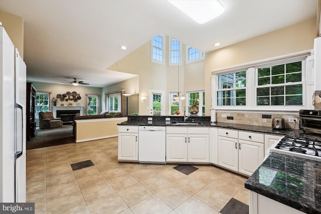 kitchen with white appliances, open floor plan, a peninsula, a fireplace, and white cabinetry