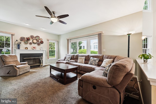 living area featuring a ceiling fan, healthy amount of natural light, a fireplace with flush hearth, and dark colored carpet