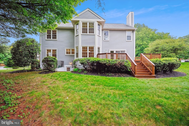rear view of property featuring a chimney, a lawn, and a deck