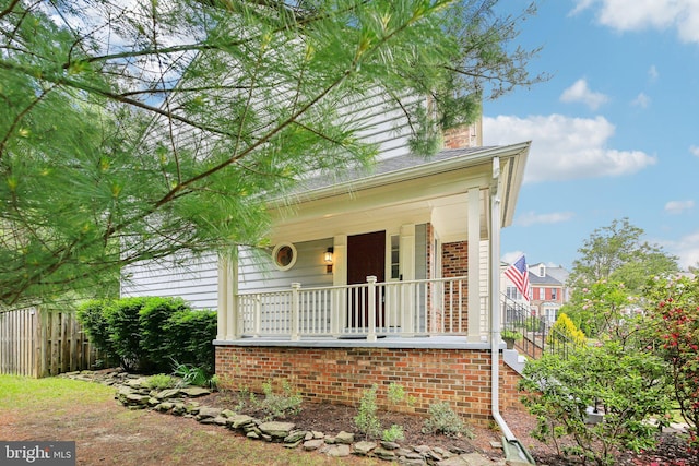 view of front of home with covered porch, fence, and brick siding