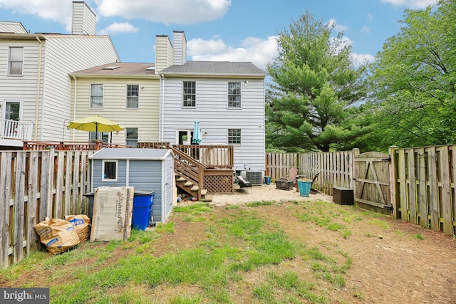 rear view of property featuring a fenced backyard, a wooden deck, a gate, a shed, and an outbuilding