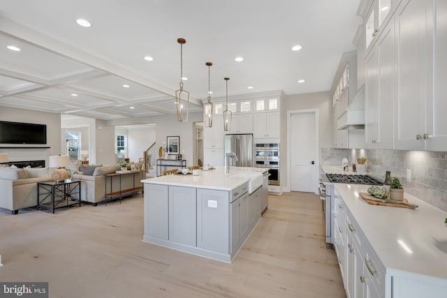 kitchen with light wood-style flooring, stainless steel appliances, open floor plan, tasteful backsplash, and coffered ceiling