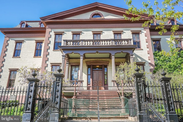view of front of house featuring a gate, brick siding, a fenced front yard, covered porch, and a balcony