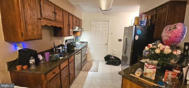 kitchen with under cabinet range hood, stainless steel appliances, light tile patterned flooring, a sink, and brown cabinetry
