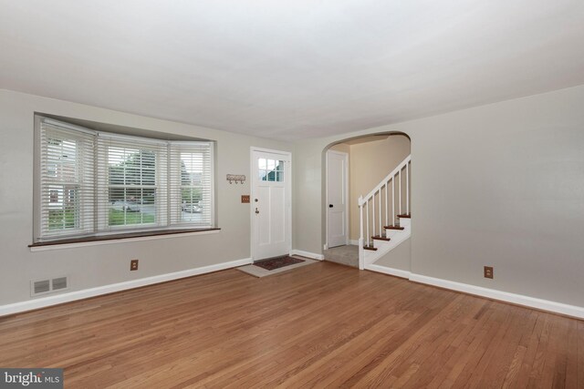 foyer with light wood finished floors, arched walkways, baseboards, and stairway