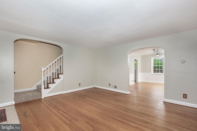 spare room with arched walkways, wood finished floors, stairway, and baseboards