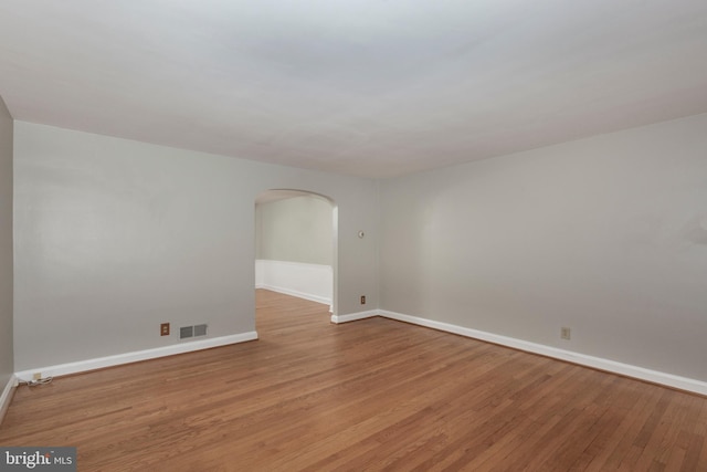 spare room featuring arched walkways, light wood-type flooring, and baseboards