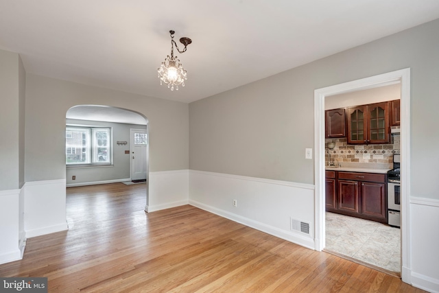unfurnished dining area with arched walkways, light wood-style flooring, a sink, a chandelier, and baseboards