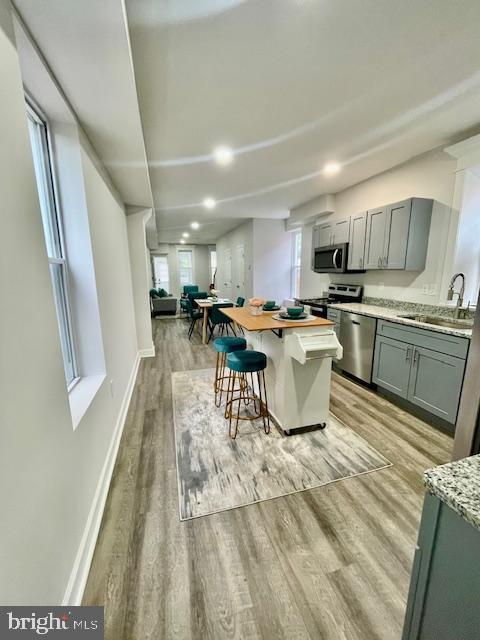 263 S Hilton St, Baltimore, MD 21229 - kitchen featuring stainless steel appliances, a sink, a breakfast bar, light wood finished floors, and plenty of natural light