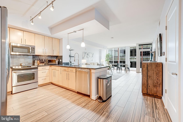 kitchen featuring stainless steel appliances, open floor plan, a peninsula, a sink, and light brown cabinets