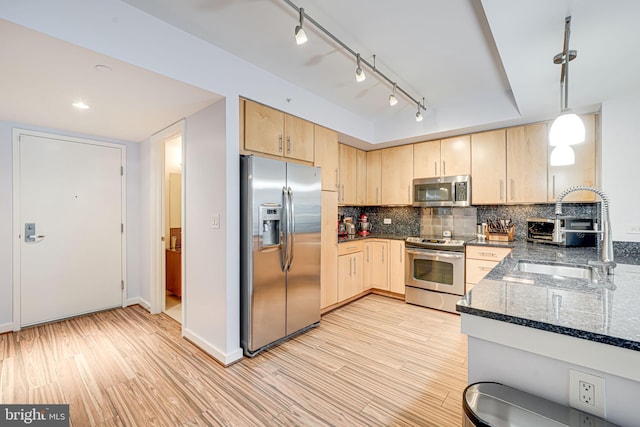 kitchen with stainless steel appliances, light brown cabinets, a sink, dark stone countertops, and light wood-type flooring