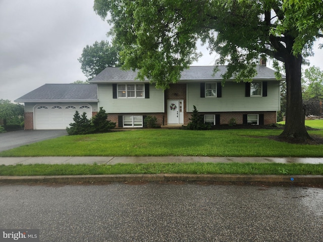 split foyer home featuring asphalt driveway, a garage, a front lawn, a chimney, and brick siding