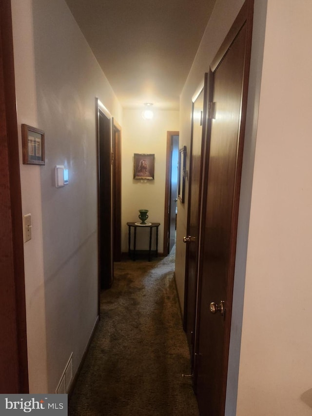 hallway with dark colored carpet and baseboards