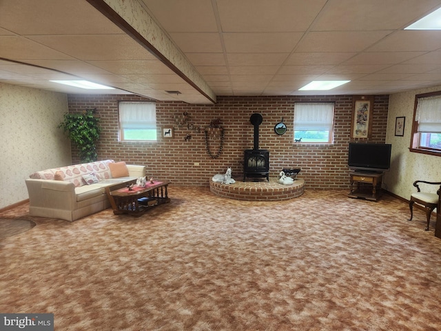 carpeted living room with a paneled ceiling, a wood stove, healthy amount of natural light, and baseboards
