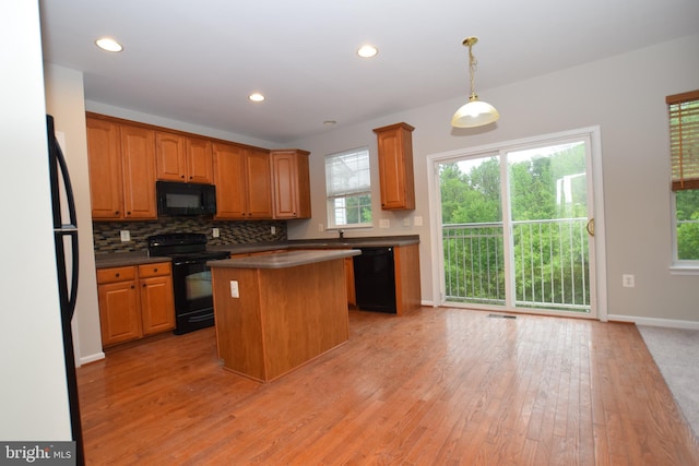 kitchen featuring black appliances, a kitchen island, light wood finished floors, decorative backsplash, and dark countertops