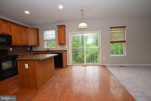kitchen featuring black appliances, a center island, dark countertops, decorative backsplash, and plenty of natural light