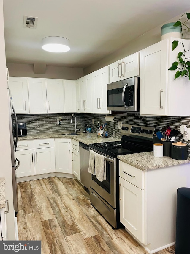kitchen featuring stainless steel appliances, a sink, decorative backsplash, white cabinets, and light wood-type flooring
