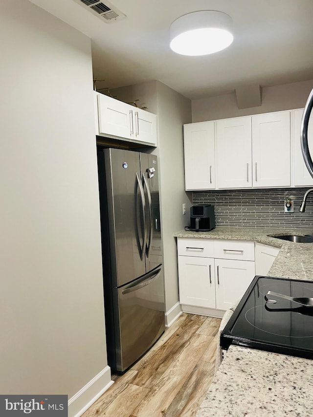 kitchen with freestanding refrigerator, a sink, light wood finished floors, black range with electric stovetop, and white cabinetry