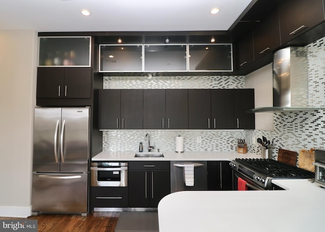 kitchen with stainless steel appliances, wall chimney exhaust hood, a sink, dark wood-style floors, and light countertops