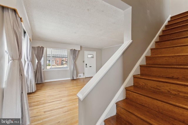 stairs featuring a textured ceiling, wood finished floors, and baseboards