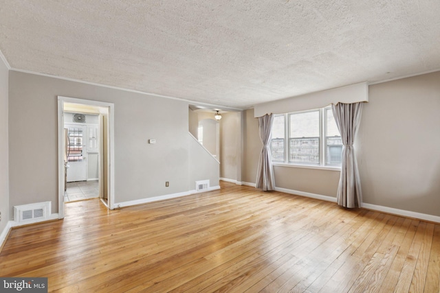 unfurnished room featuring a textured ceiling, light wood-style flooring, baseboards, and crown molding